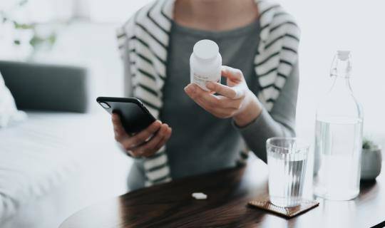 Woman looks at pill bottle and her phone