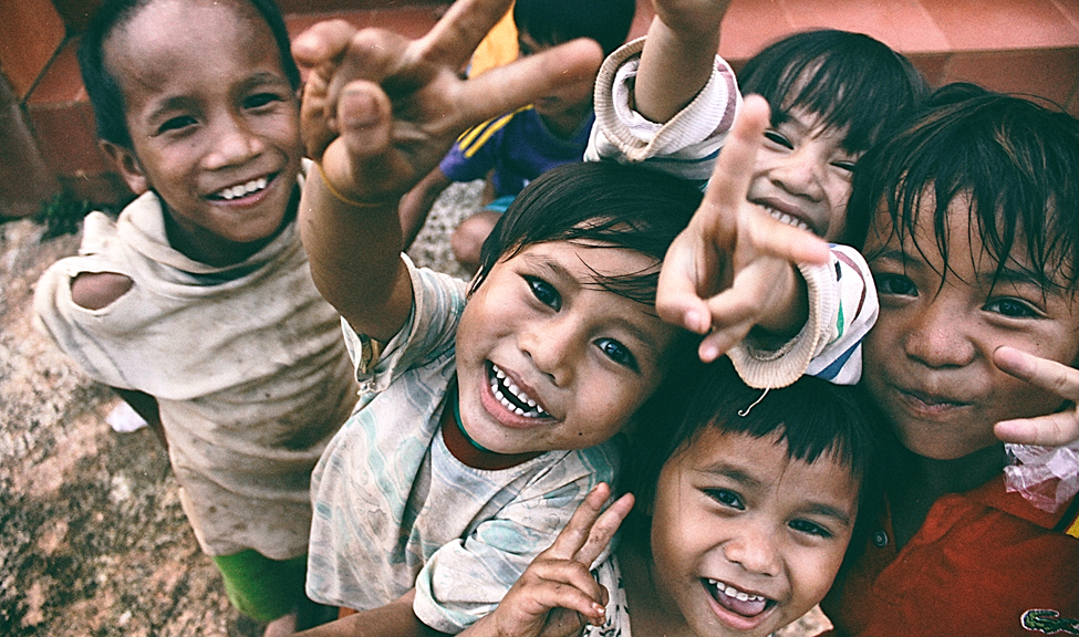 Young children of different races smiling and making peace signs with their hands