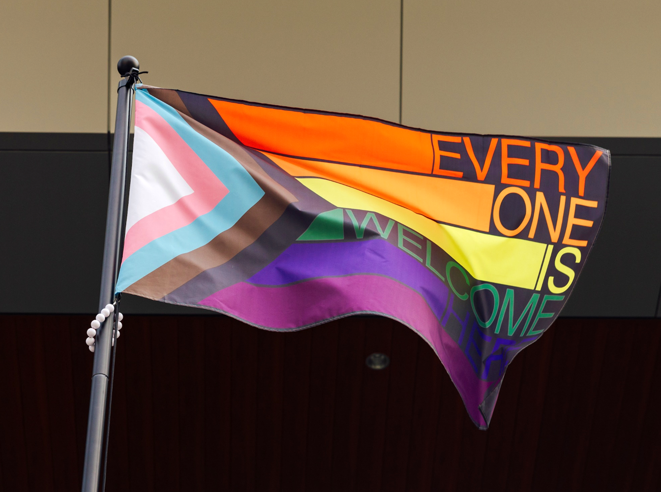 A Pride Progress flag that reads "Every one is welcome here" with each word in a different color of the rainbow
