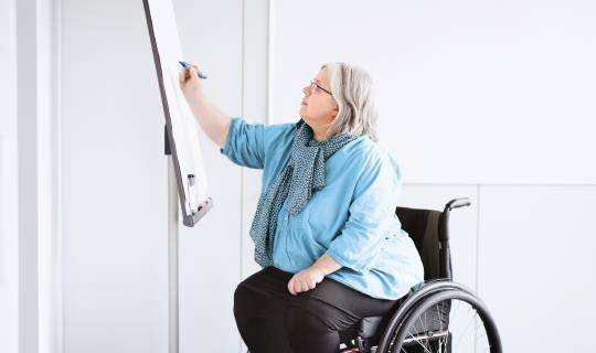 Middle-aged woman in wheelchair draws on a white board