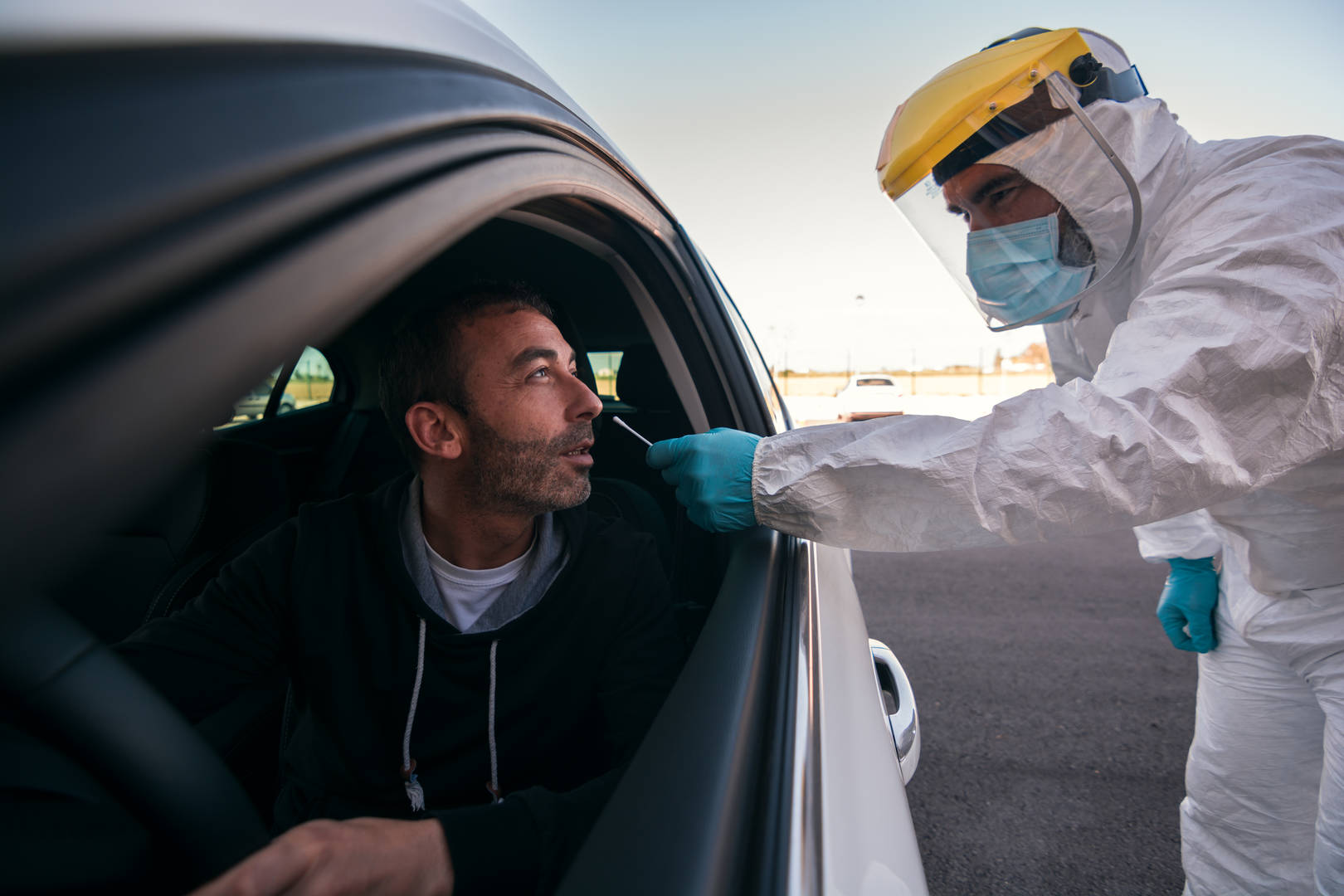 Lab tech in protective gear checks patient in car