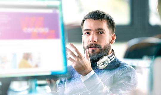 Man with beard and headphones sitting in front of computer in office