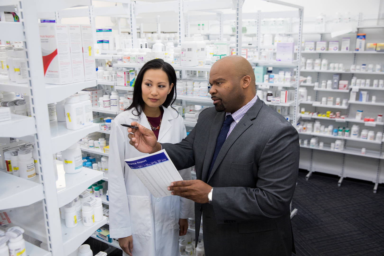 A Good Neighbor Pharmacy business coach reviews inventory behind the counter with a pharmacist
