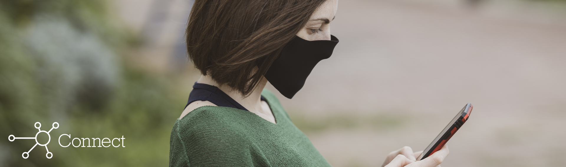 A woman wearing a face mask reading a text message from her pharmacist on her phone