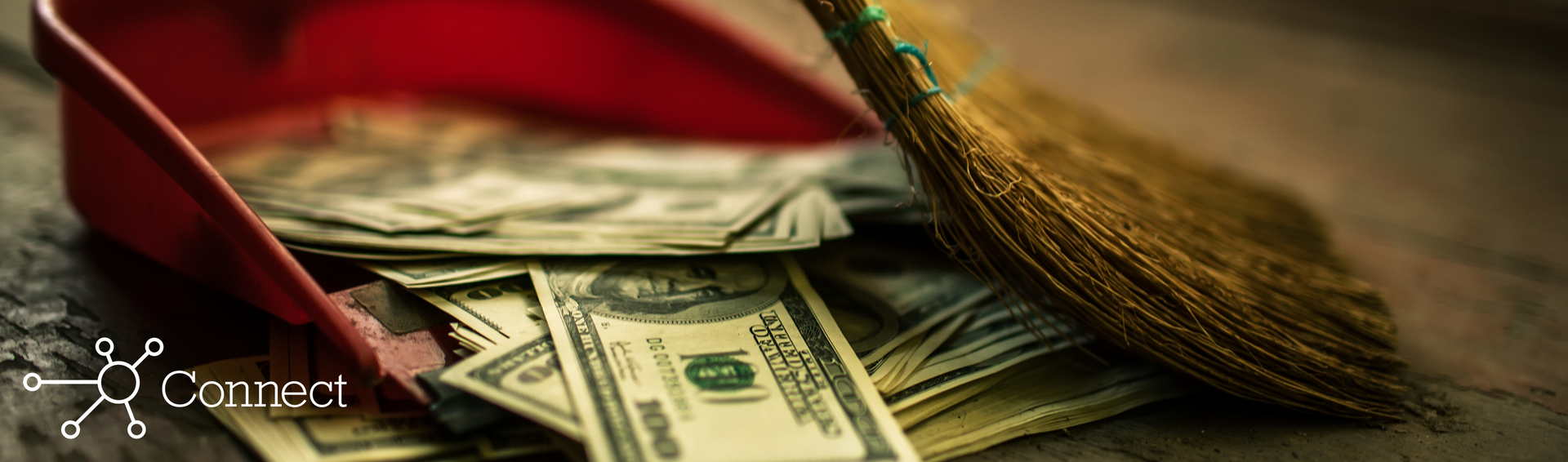 Someone using a broom to sweep dollar bills into a dust pan