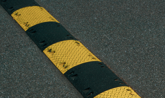 A yellow and black striped speed bump on asphalt