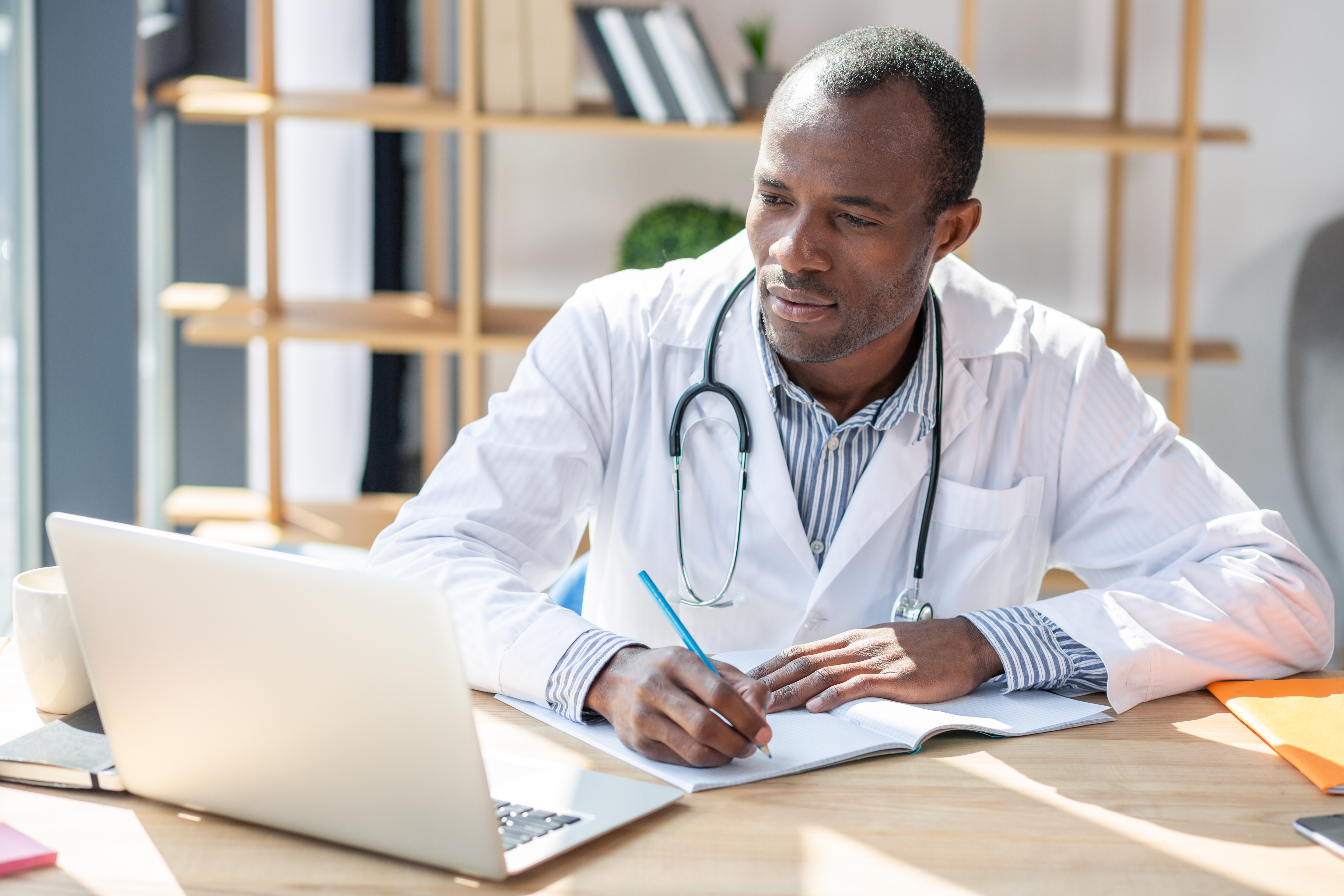 Physician looks at laptop and takes notes