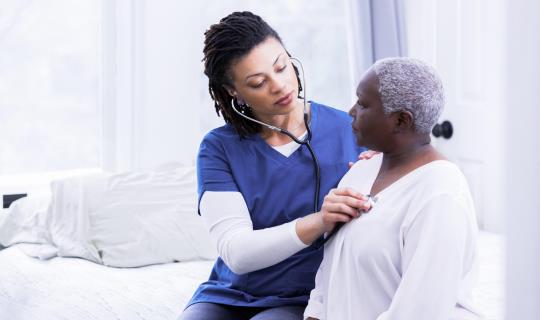 Black female nurse uses stethoscope on older Black female patient