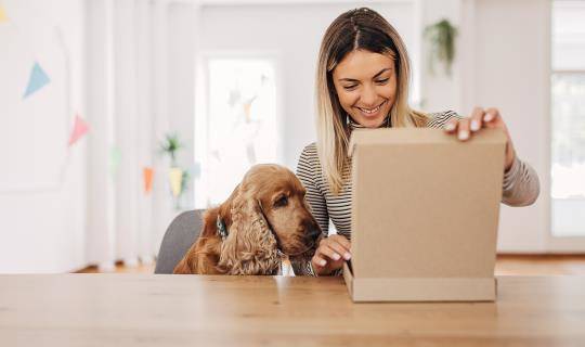 Woman opens package as dog looks on