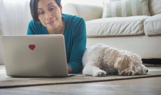 Black woman looks at laptop with small dog by her side