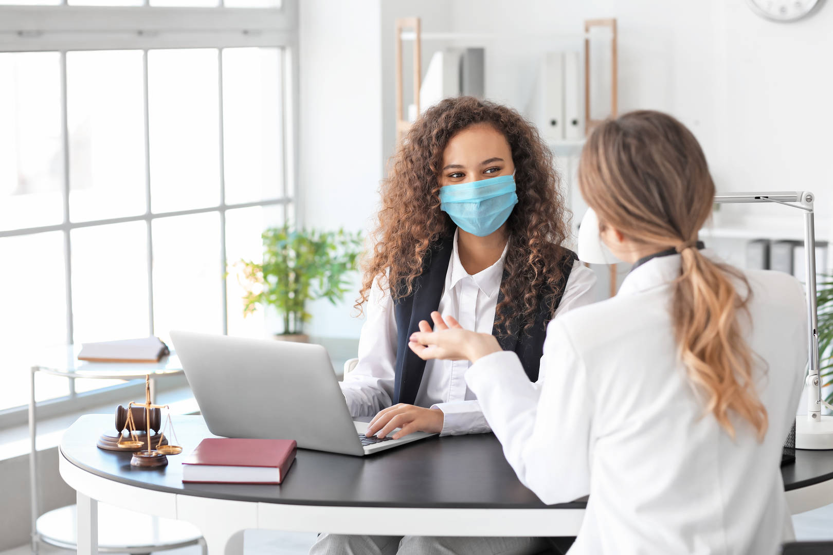 2 healthcare professionals wearing face masks and talking over laptop