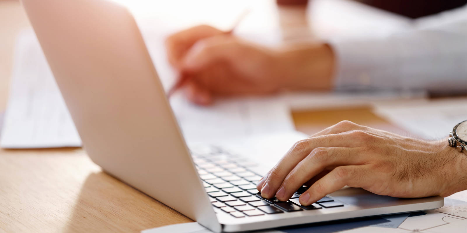 person's hands working on laptop and taking notes