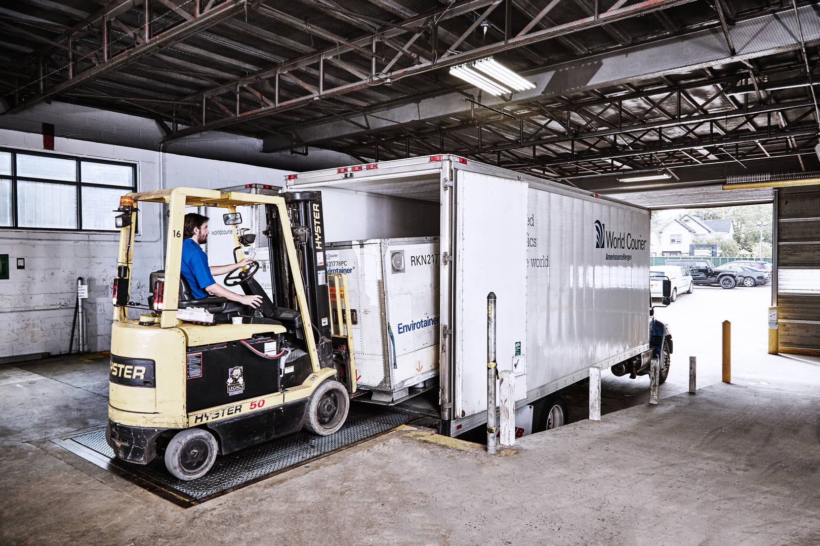 A forklift loads a shipping container into a World Courier truck at a loading dock.