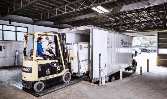 A forklift loads a shipping container into a World Courier truck at a loading dock.