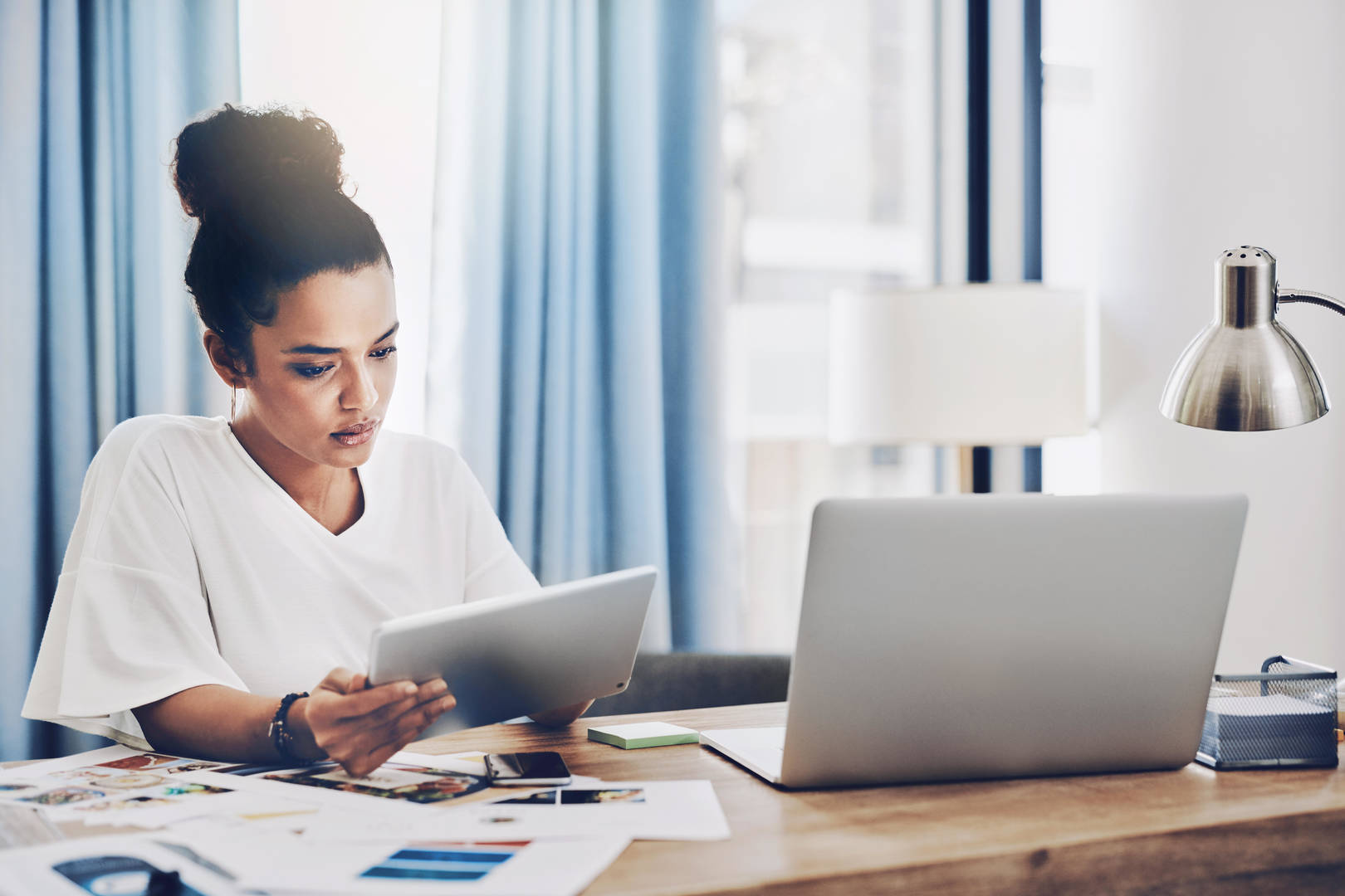 A young Black women looks at a tablet at her desk in a home office set-up