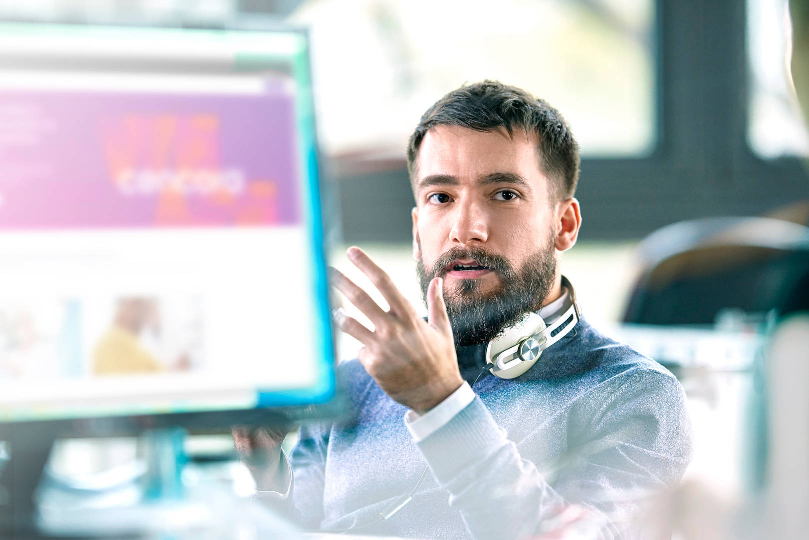 Man with beard and headphones sitting in front of computer in office