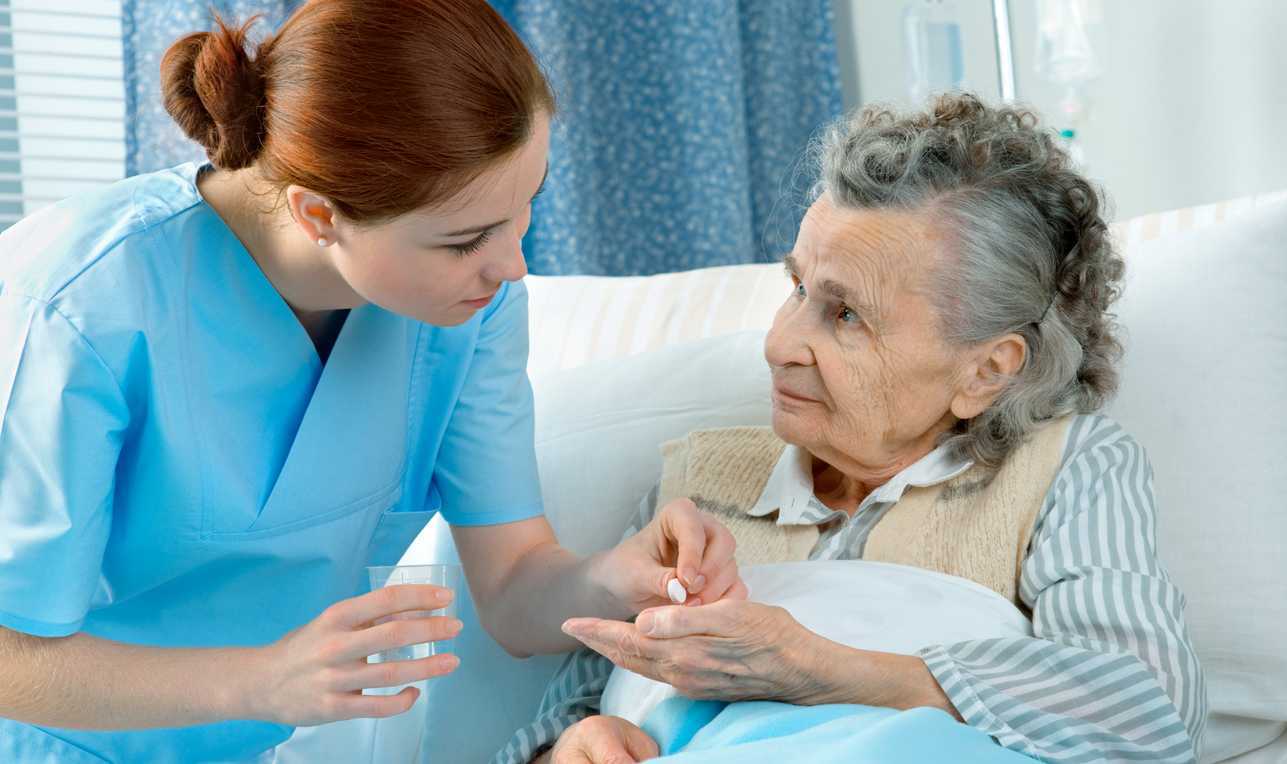 A female nurse handing medication to a woman laying in a hospital bed